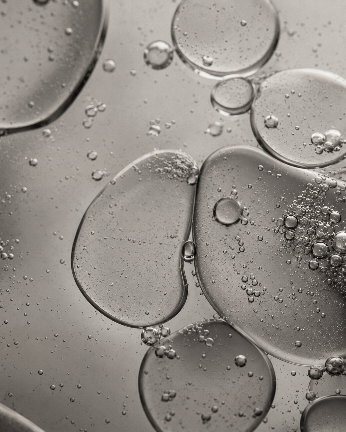 Abstract close-up of translucent droplets and bubbles on a smoky gray surface.